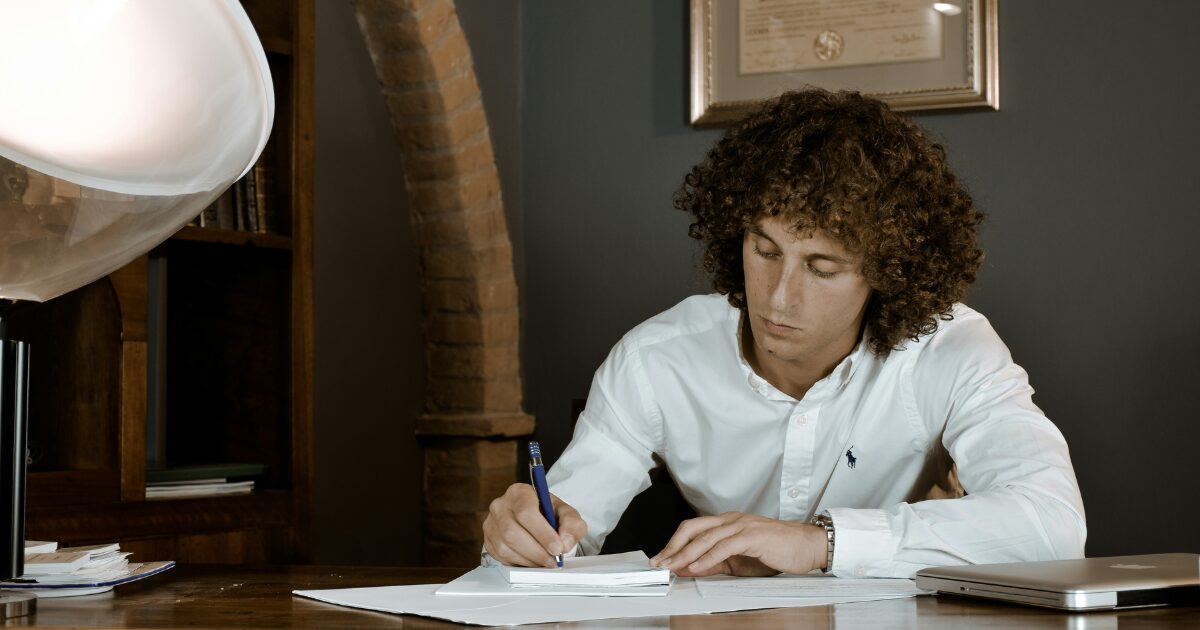 333 Caucasian man wearing a white long-sleeved shirt, writing something on a piece of paper.