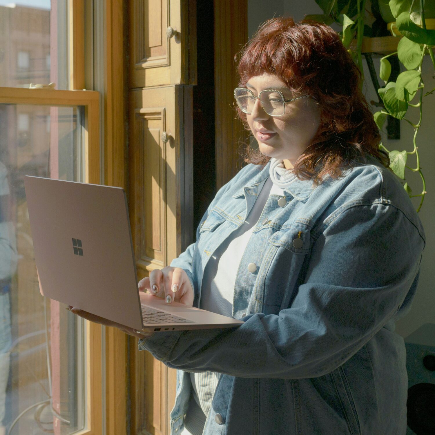 Young Caucasian woman wearing a jean jacket, holder her laptop as she scrolls on it.