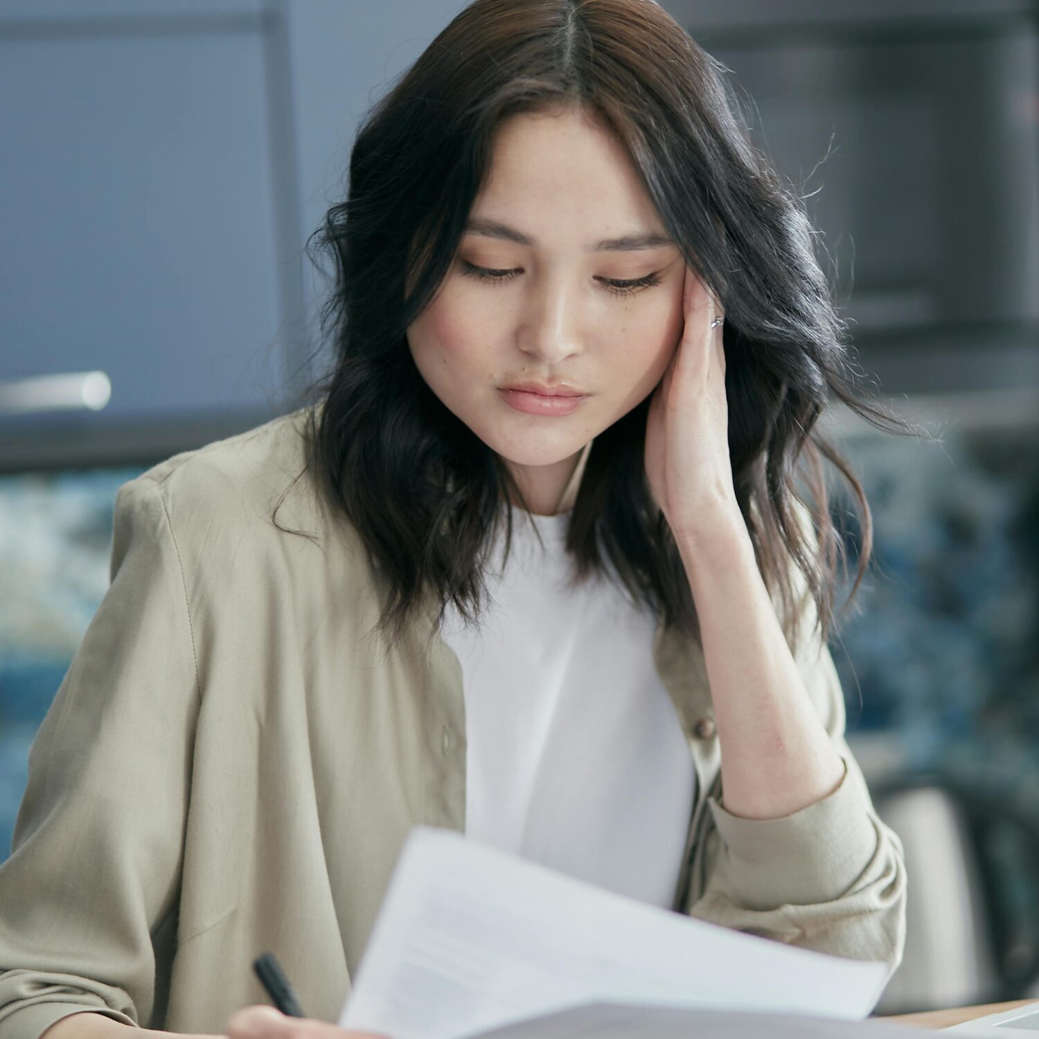Young East Asian woman looking over a document, wearing a beige blazer over a white shirt.