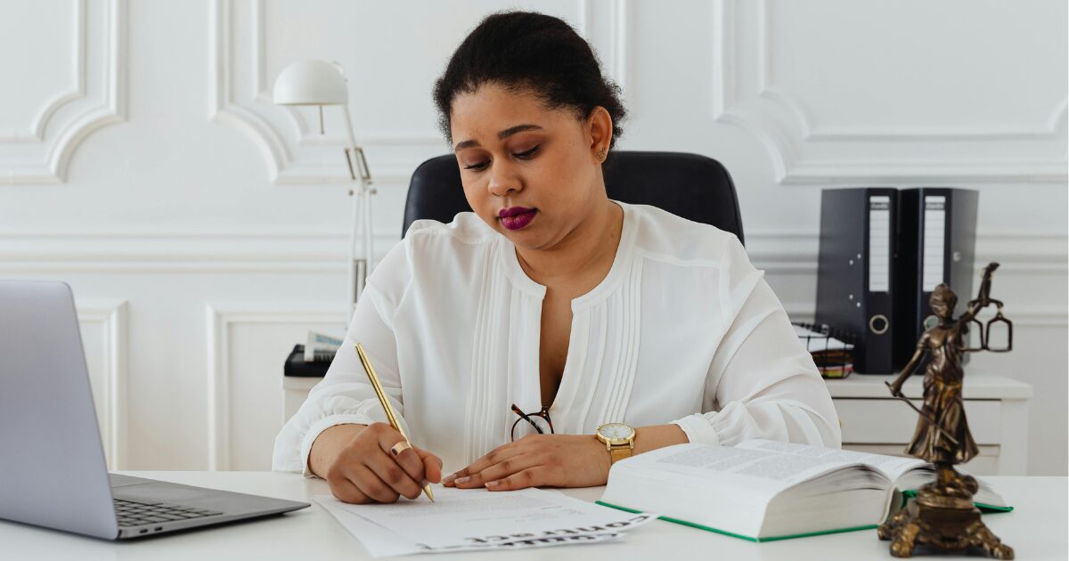 A Black woman with the scales of justice on her desk, notarizing a legal document.