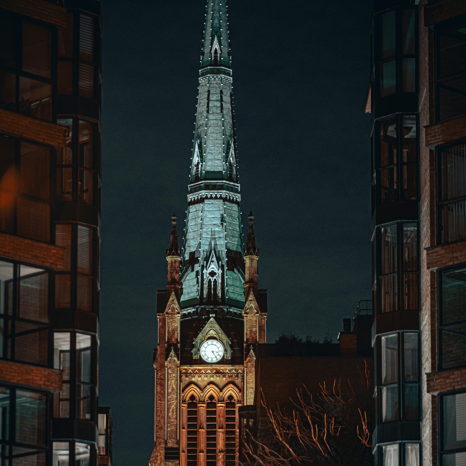 A grey and brown peace tower with a clock in the front with two buildings on each side. The sky is dark as its nighttime.