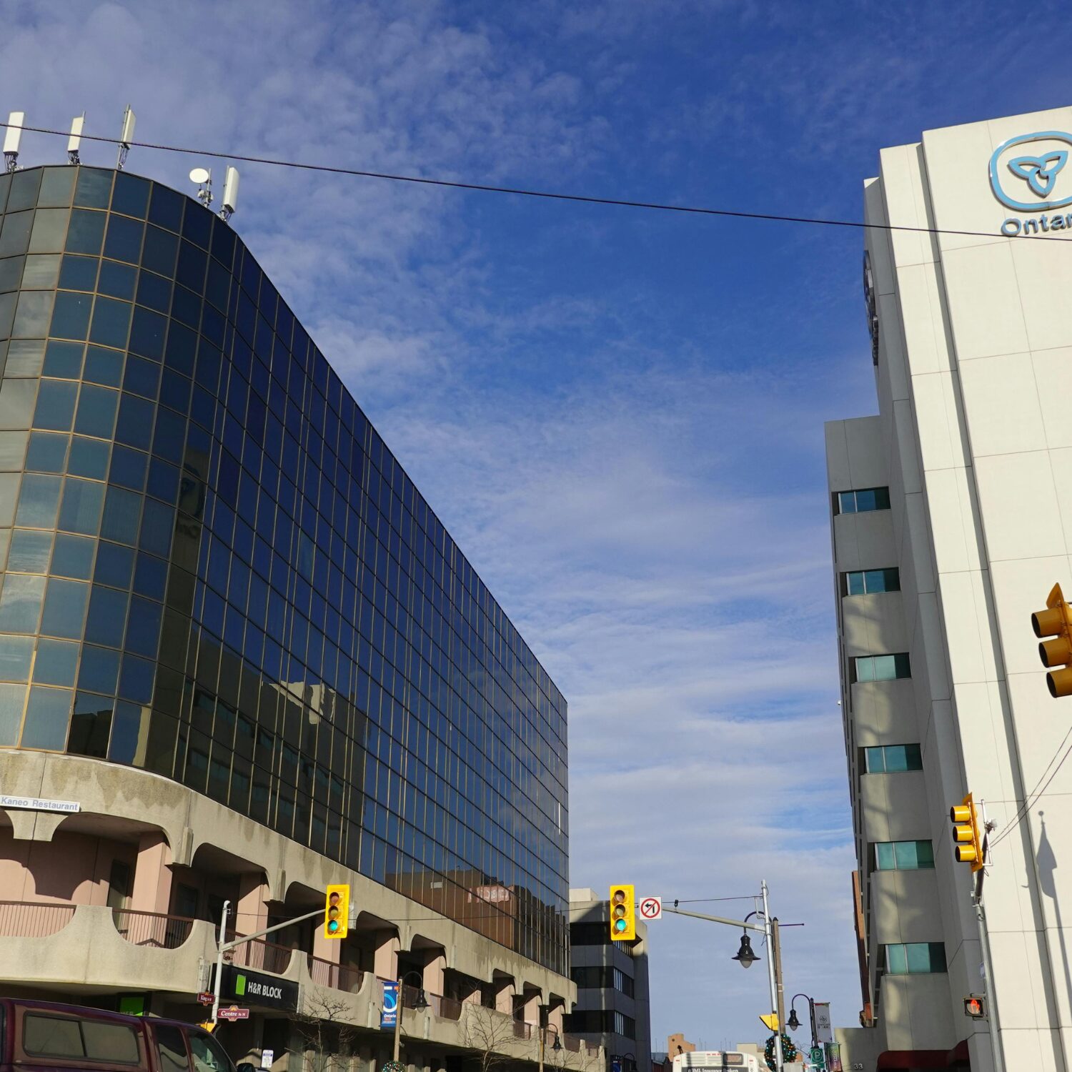 A street view of Oshawa, Ontario with a dark grey glass building to the right and a blue sky above.
