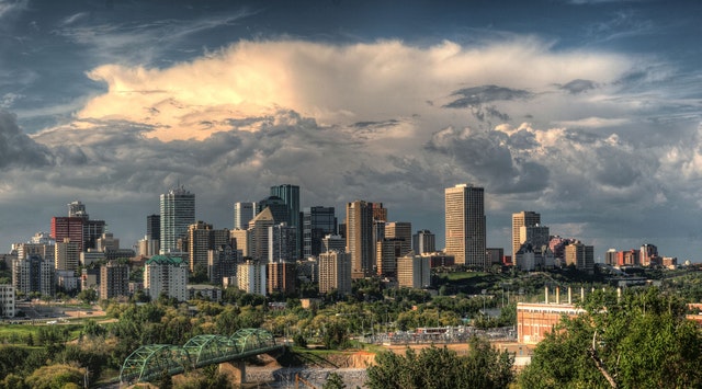 The Edmonton skyline with dark gray clouds in the background, and green trees at the front.