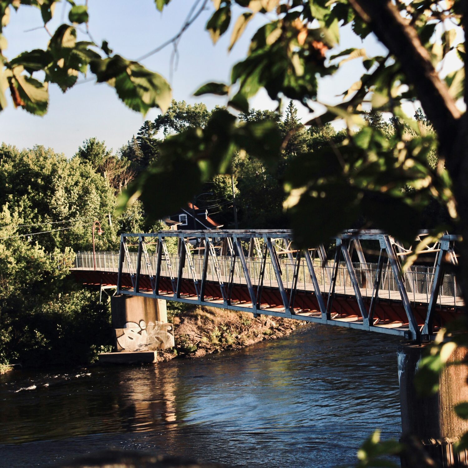 A bridge in Gatineau with water flowing beneath it. It's surrounded by green trees.
