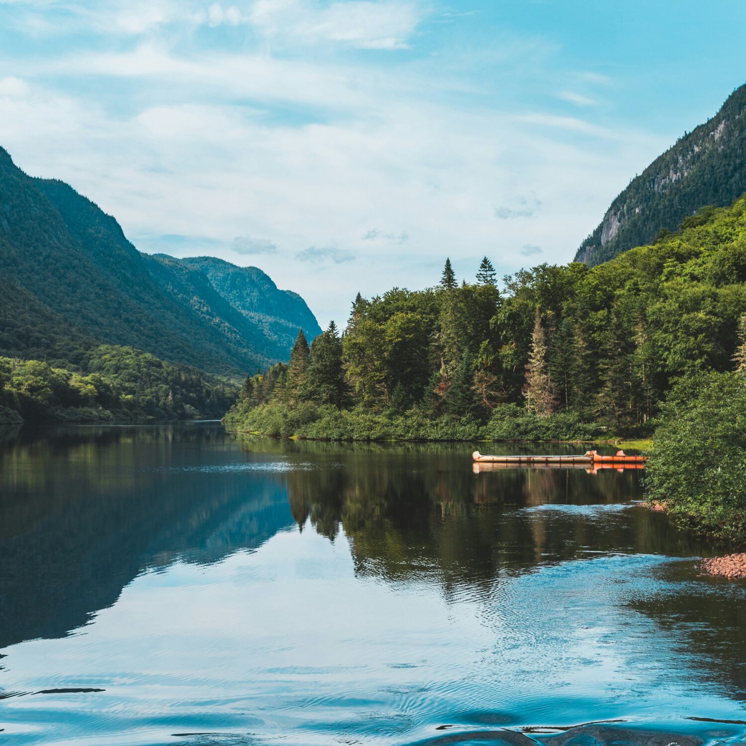 A lake in Quebec, surrounded by evergreen trees and mountains. There is a dock in the water.