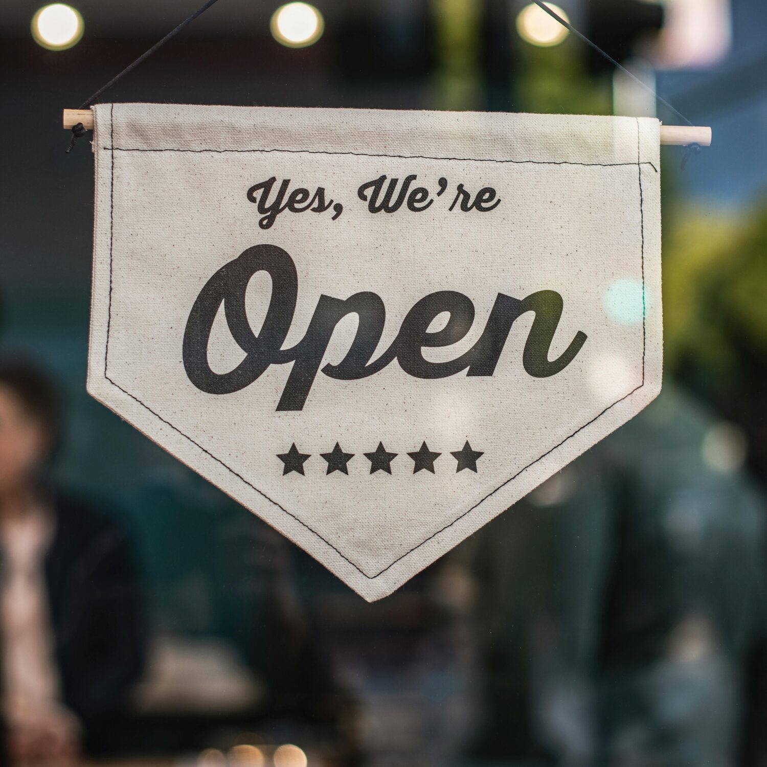 A white sign hanging in a window with black writing that says "Yes, we're open"