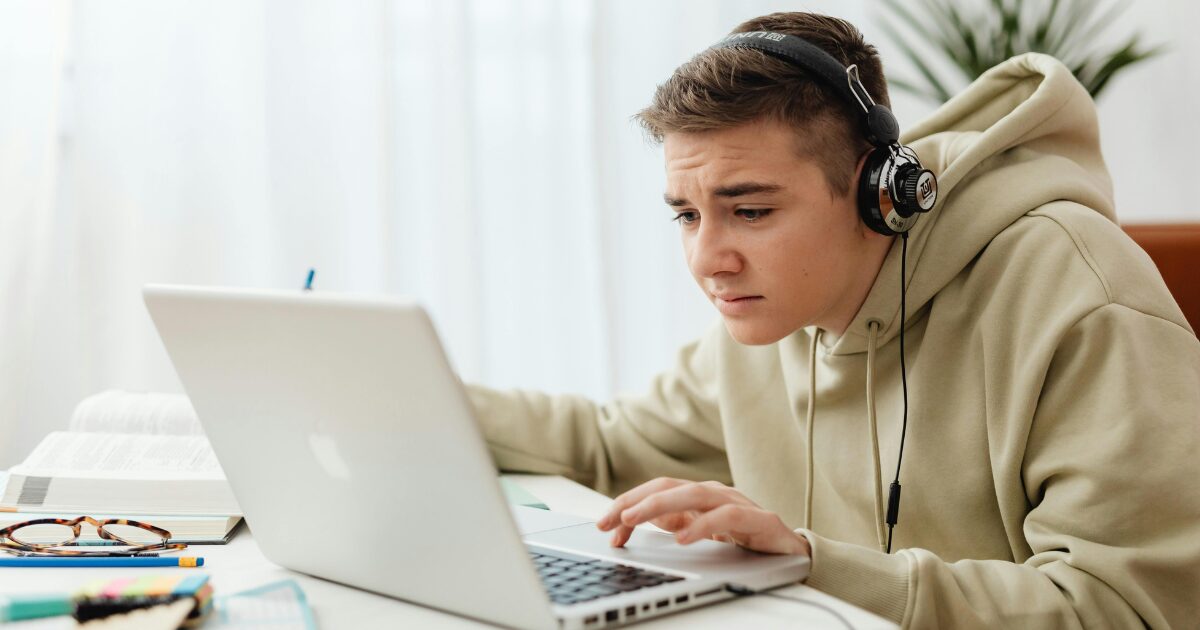 A Caucasian man wearing a beige hoodie works on his laptop.