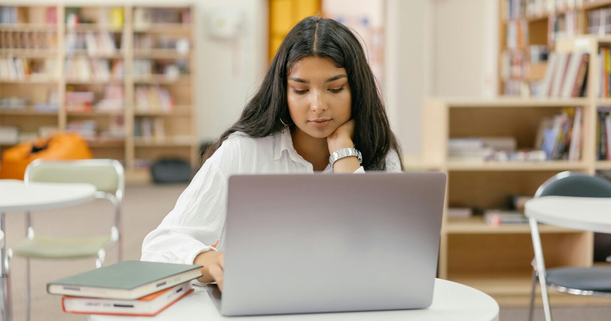 A South Asian woman wearing a white blouse uses her laptop.