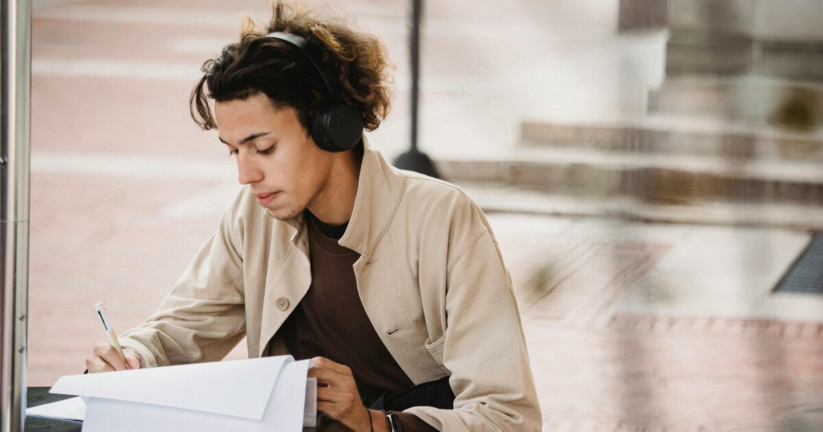 A Caucasian man wearing a beige coat writes on his papers.