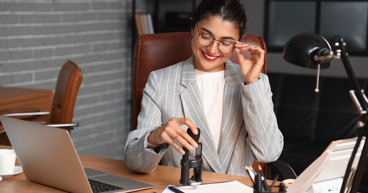 Young female notary with glasses stamping a document with an open laptop