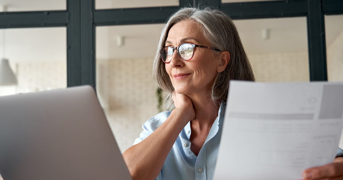 Older woman holding document while using laptop