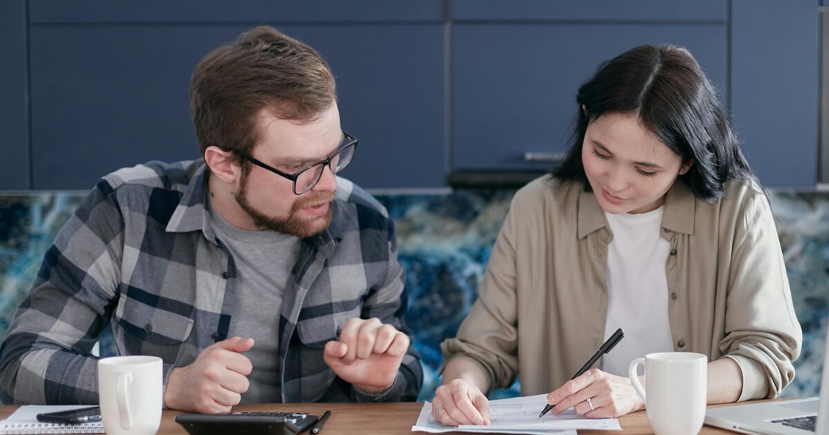 Untitled design (6) A man and a woman sitting at a wood table going over documents to be notarized.