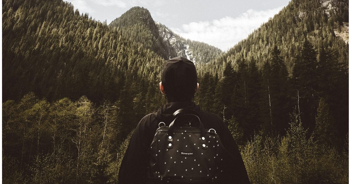 A male tourist wearing a black cap and a black backpack, on a hike in the Canadian mountains