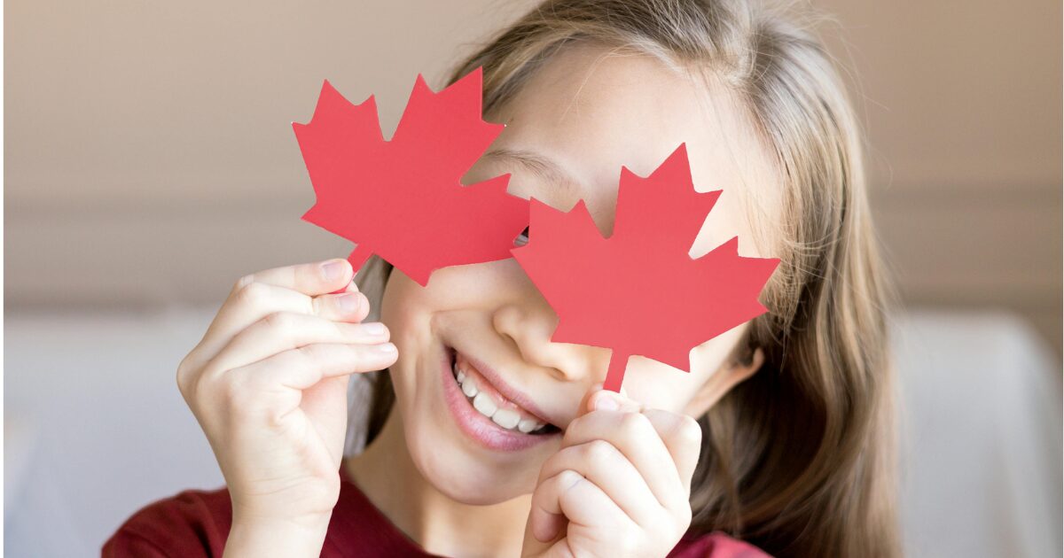 Young Mexican girl smiling, holding up two maple leaves against her eyes