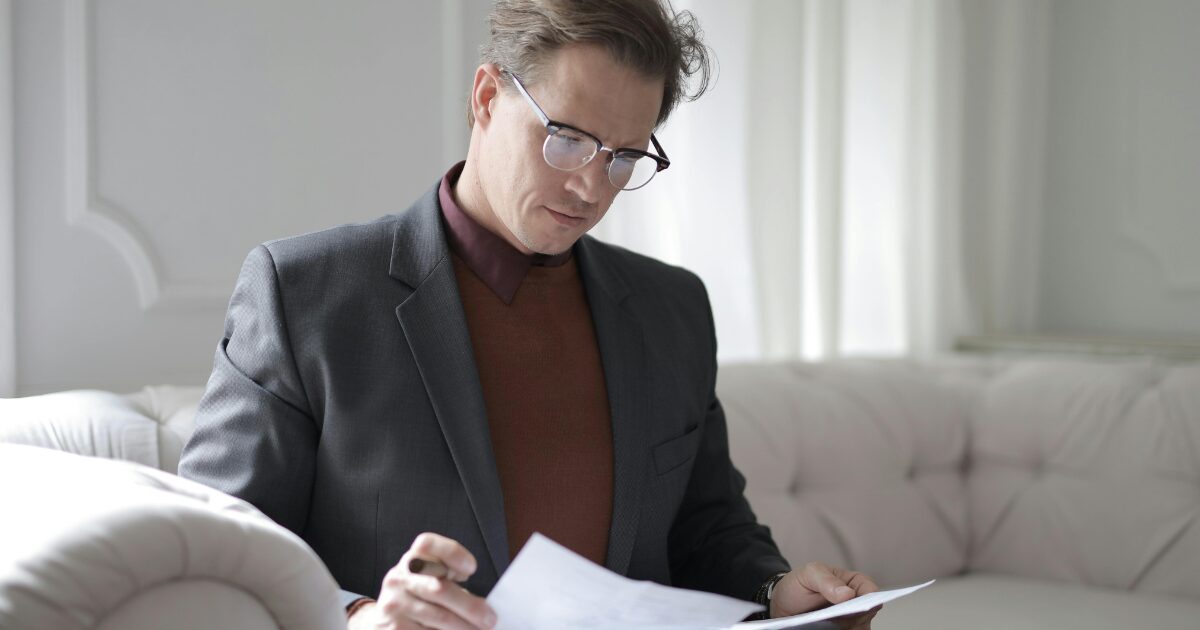 A middle-aged man sitting on his couch, reviewing documents required to register a company vehicle.