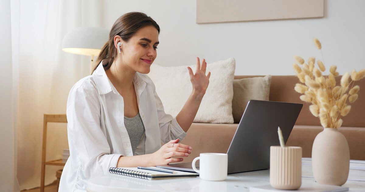 A young Caucasian woman in a living room, on her lap top at a virtual appointment.