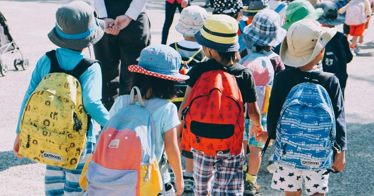 A group of young children wearing sunhats and backpacks.