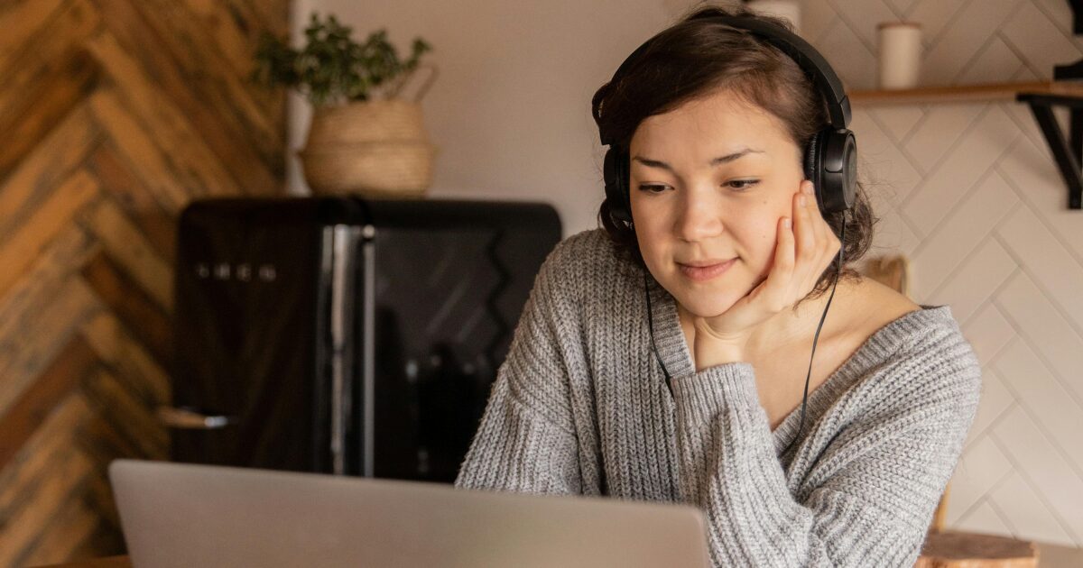 A young woman on her laptop, on a video call to get documents notarized, wearing headphones.
