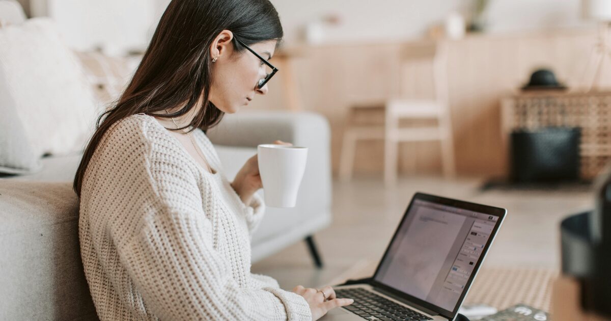 A young Caucasian woman sitting with a laptop writing.