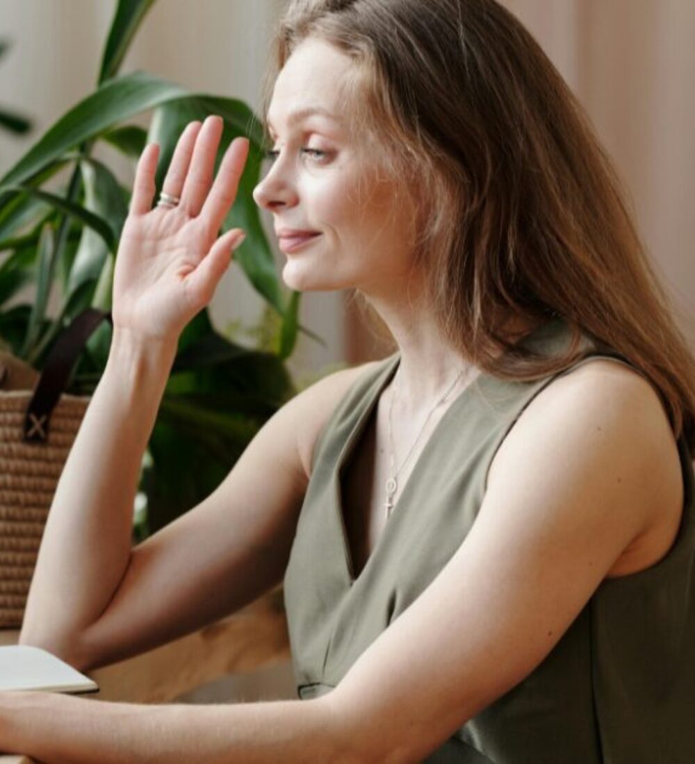 A middle-aged woman in an olive green vest, with her right hand up as she takes an oath.