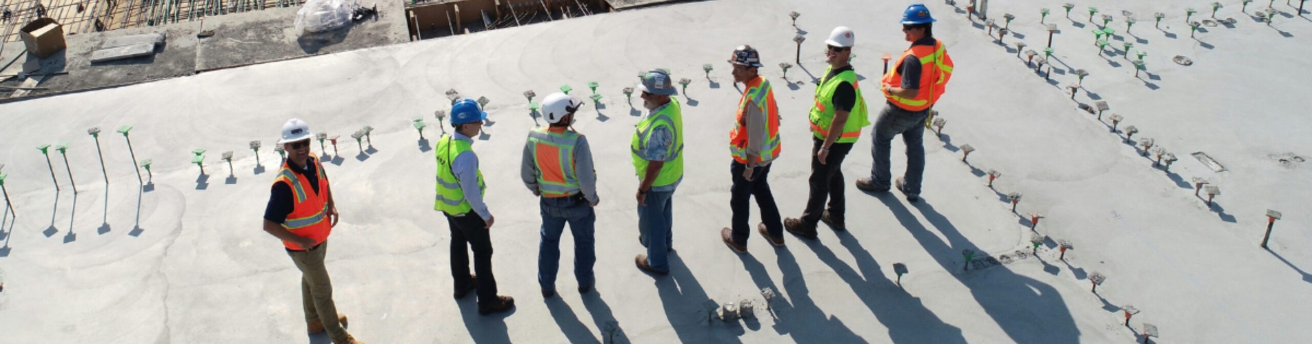 A lineup of construction workers wearing blue jeans, hard hats, and high-visibility vests.