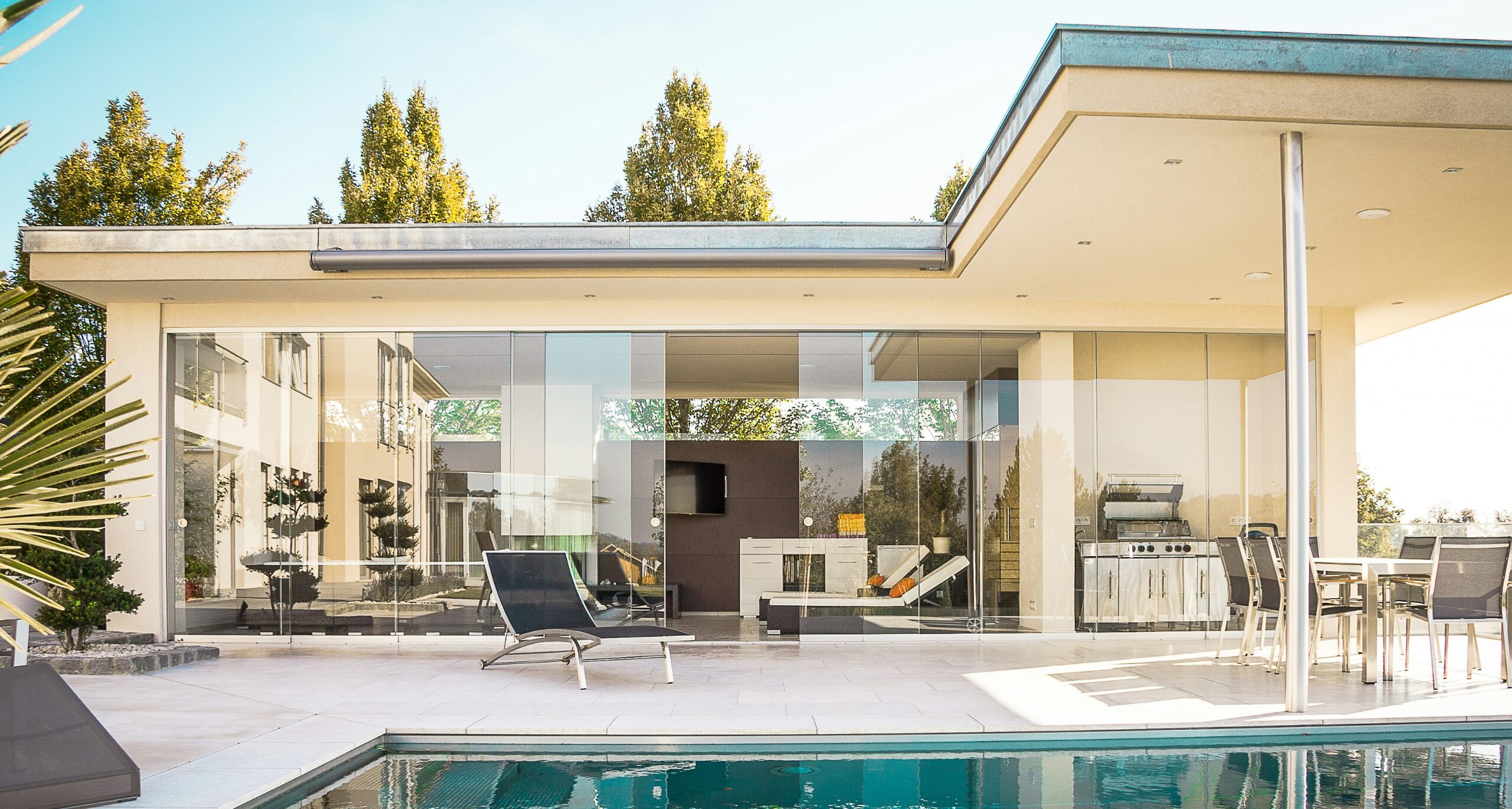 A modern house with glass walls and a swimming pool on a bright sunny day.