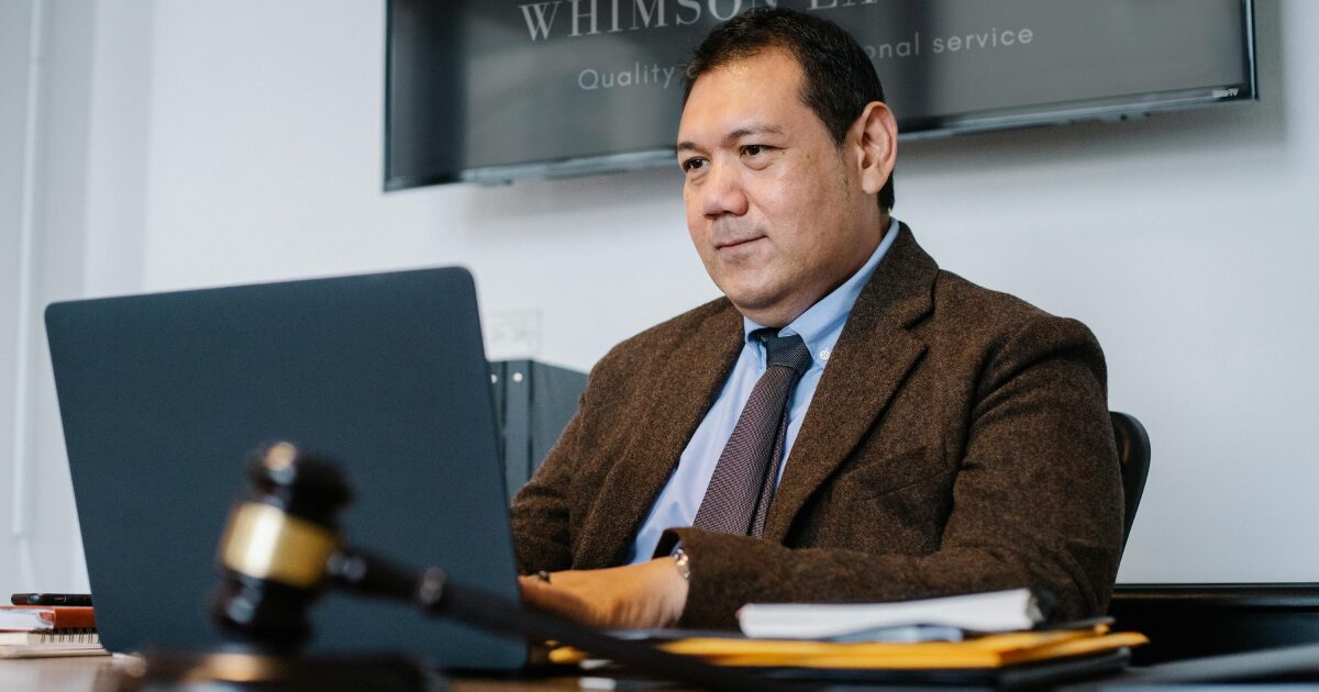 A middle-aged Hispanic male notary public typing on a laptop, with a gavel on his desk.