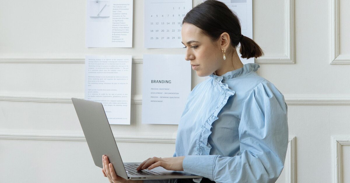 A young Caucasia woman with a pony tail, in a blue blouse typing on her laptop.