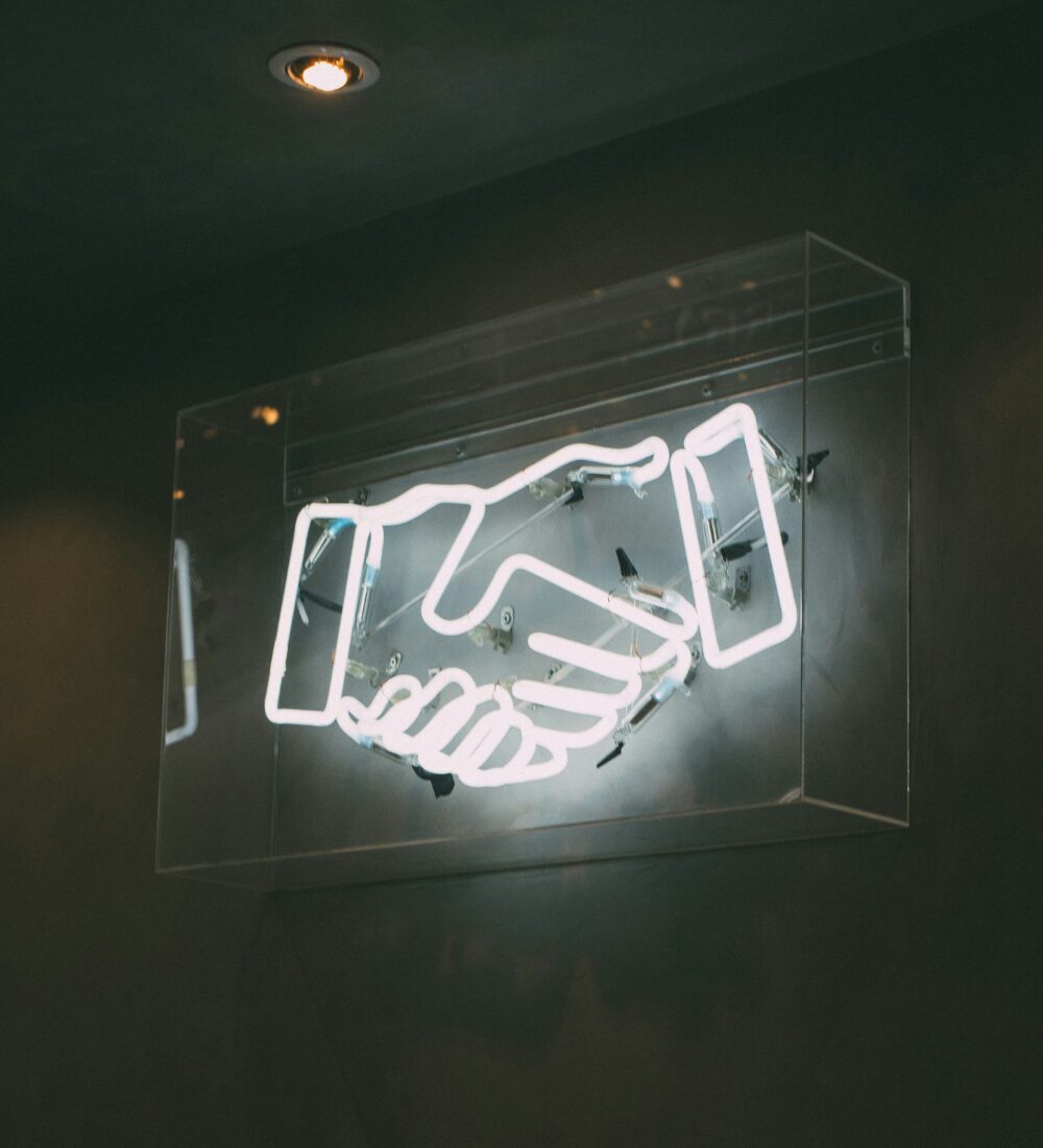 White neon sign in the shape of a handshake, on a black wall.