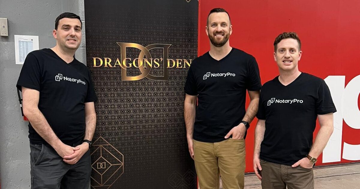 3 young male NotaryPro executives at CBC studios, posing in front of a pull-up banner with the Dragons' Den logo on it.