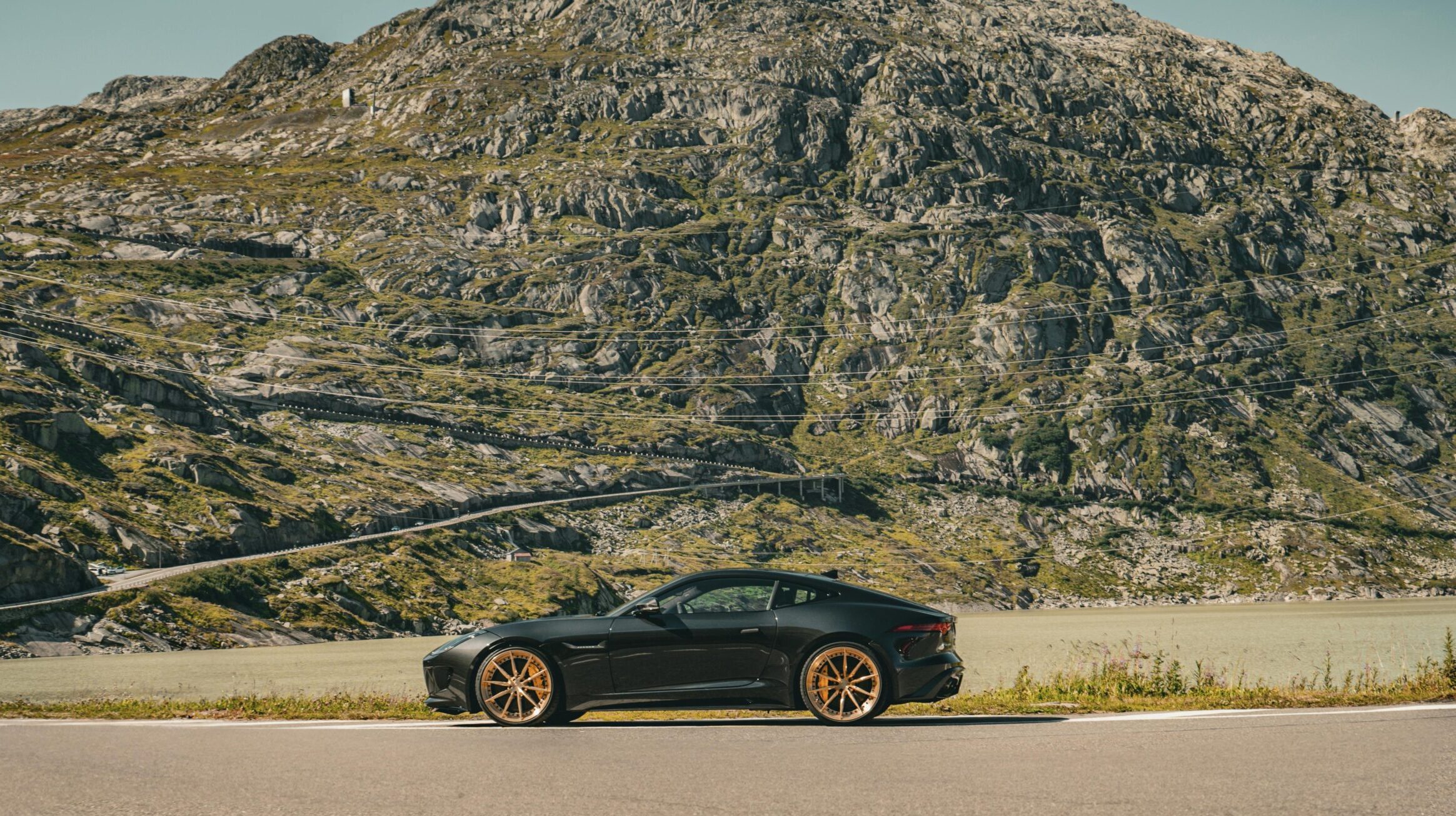 A black car parked on the side of the road, with a large mountain behind it.
