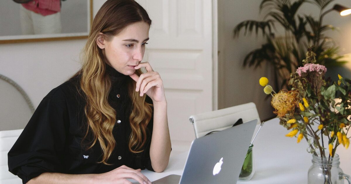 223 Young Caucasian woman wearing a black blouse, reading something on a MacBook laptop.