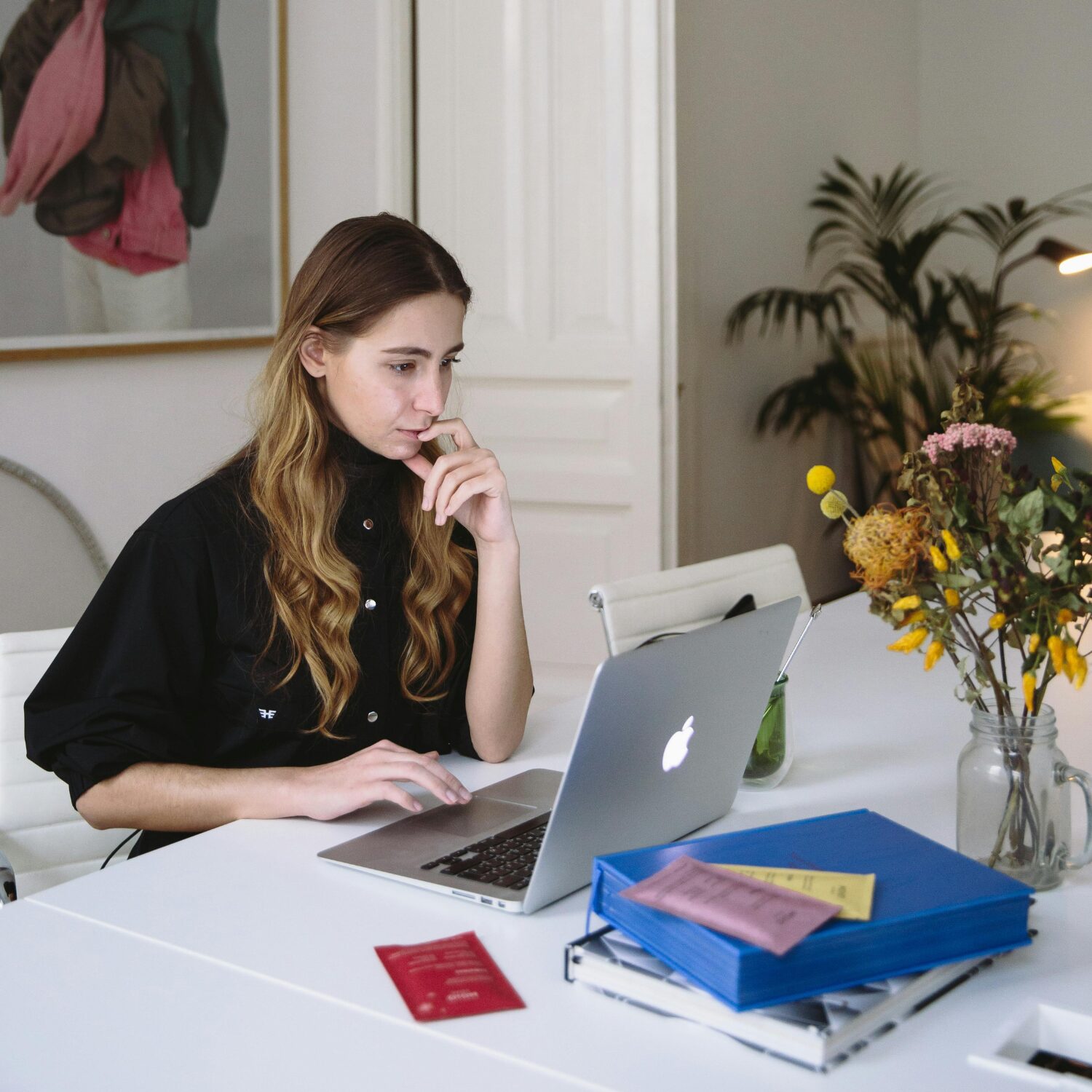 Young Caucasian woman wearing a black blouse, reading something on a MacBook laptop.