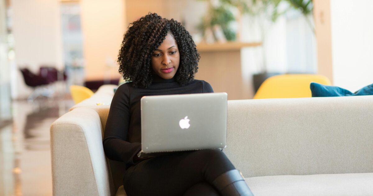 242 An African American woman with afro hairstyle is sitting on a sofa with a laptop on her lap.