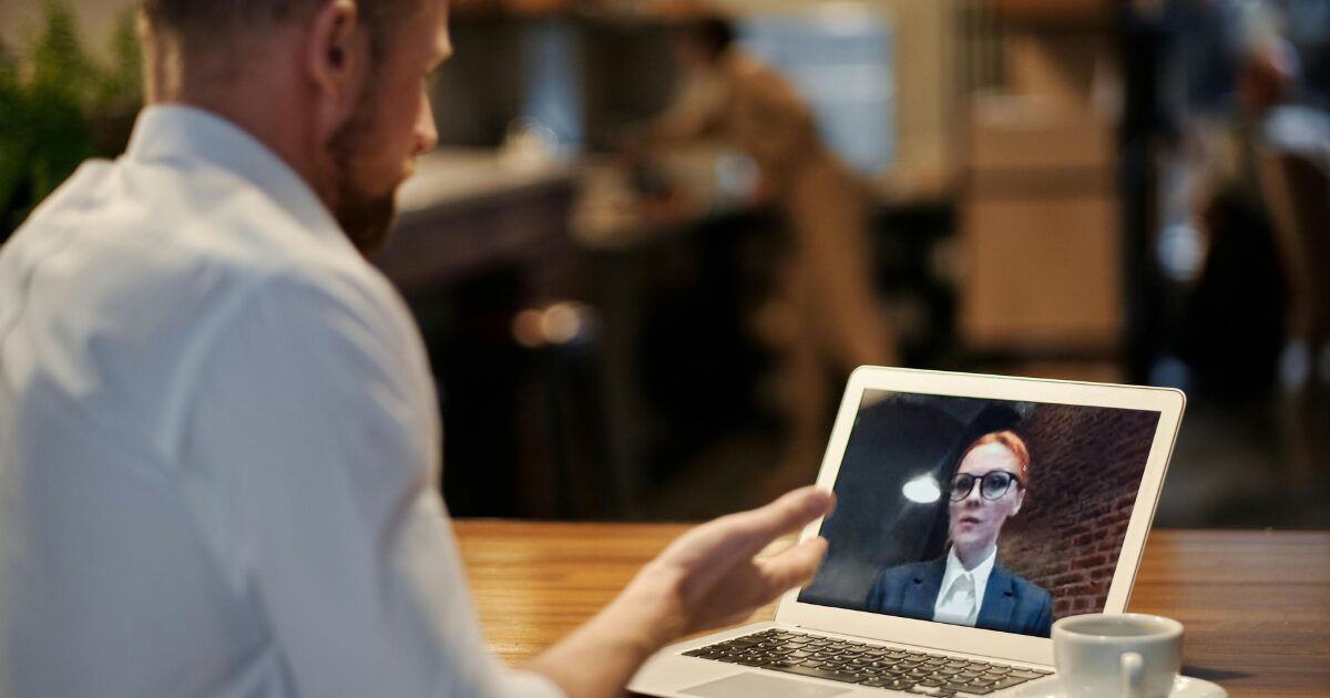 243 An American man is having a video conference with an American woman via laptop. The American man is sitting on a cafe with a cup of coffee and a laptop.