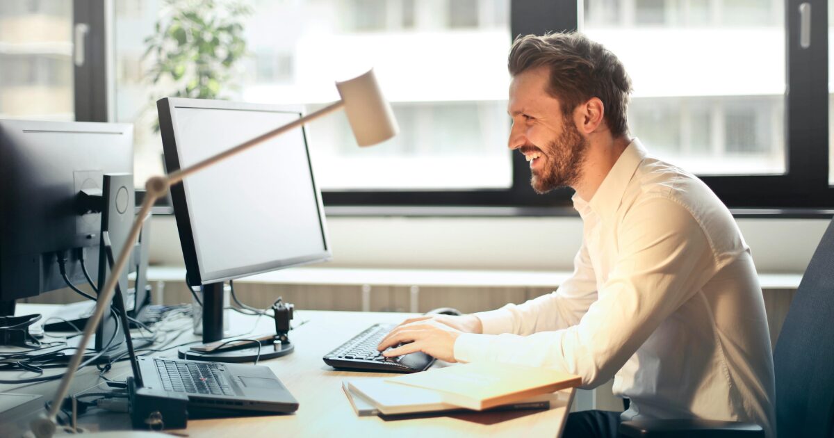245 An American business man is smiling while sitting at his office in front of his computer.