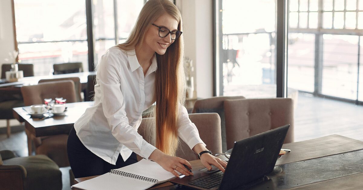 246 An American woman with red hair is smiling as she uses her laptop while standing in a cafe.