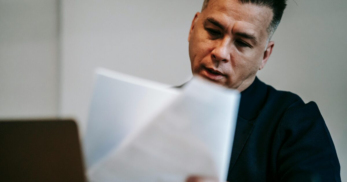 A Caucasian man wearing a black shirt reading documents he’s holding