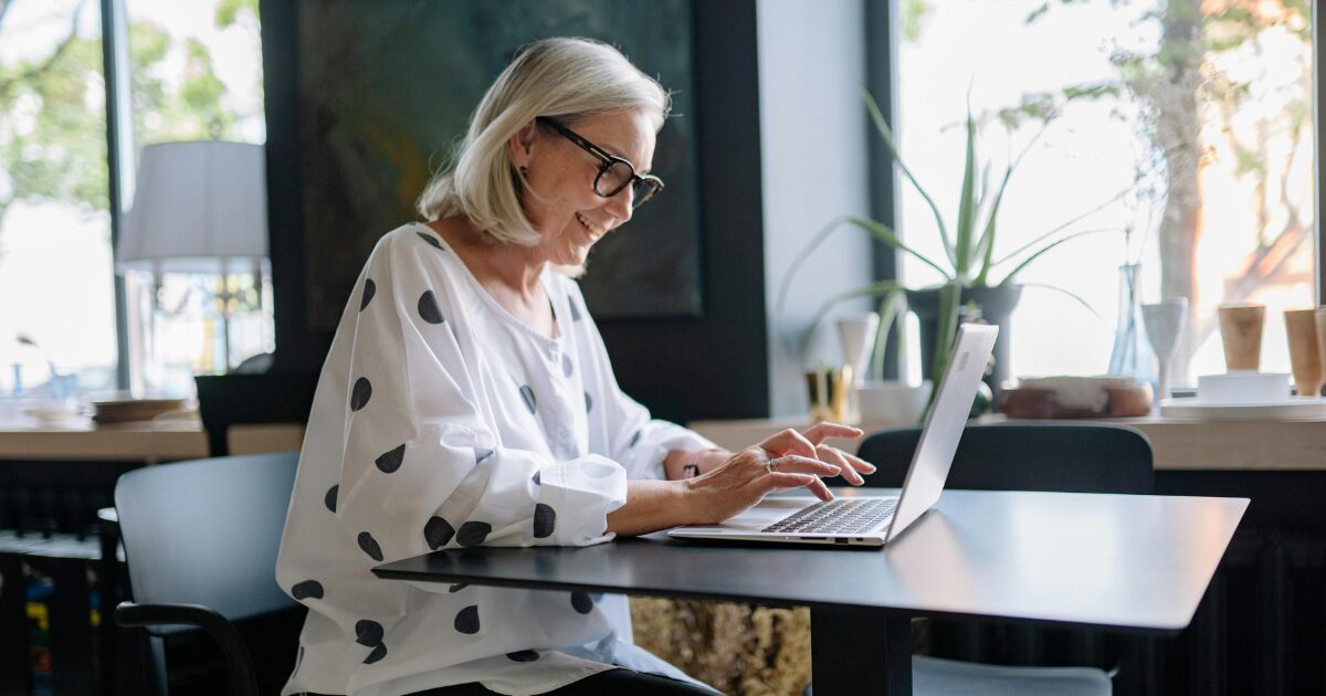 257 An elderly Caucasian woman in white and polka dot blouse, smiling while typing on her laptop