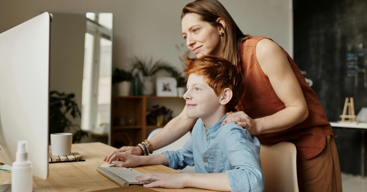 261 A Caucasian woman and a young Caucasian boy, smiling while looking at a computer monitor. The woman is wearing a brown sleeveless blouse, while the boy is wearing a blue blouse.