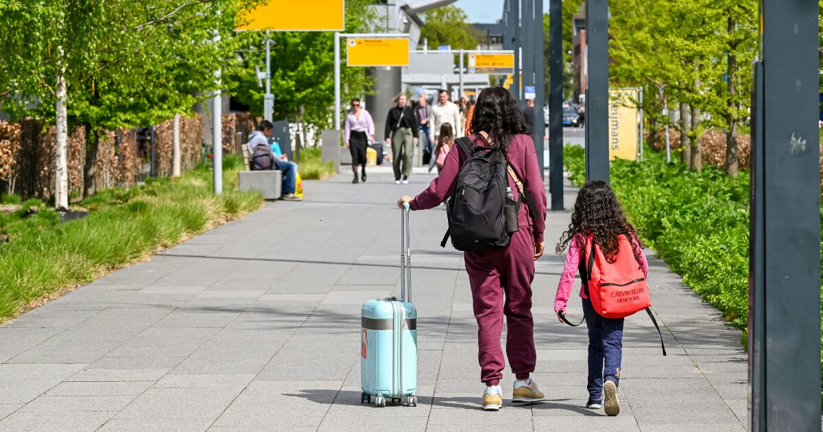 265 A woman and a young girl walking down the street wearing backpacks. The woman is holding a suitcase, and they’re facing away from the camera