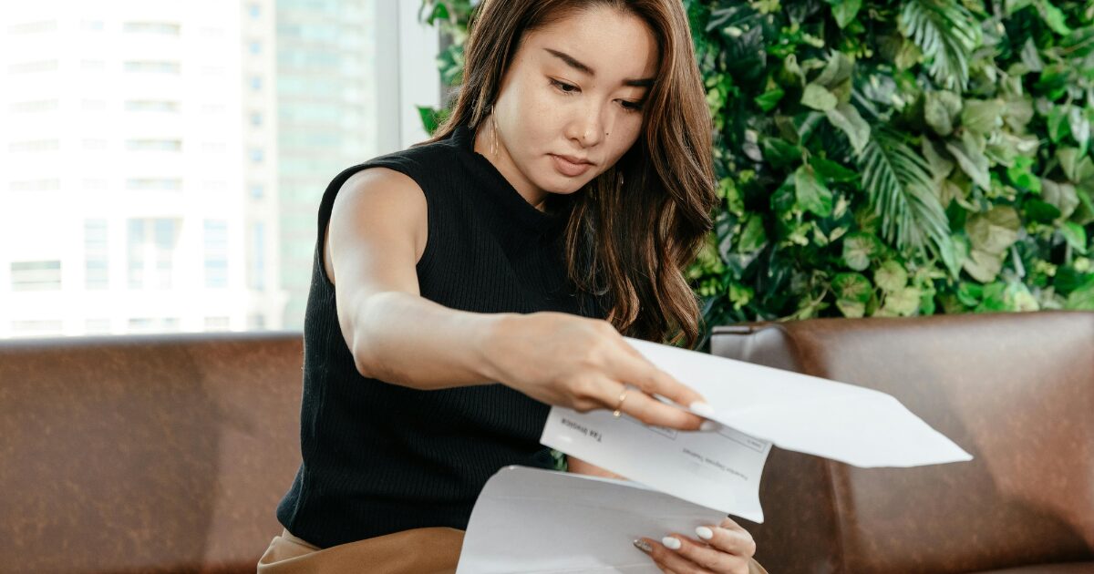 271 An East Asian woman sitting on a brown sofa while flipping through some documents she’s holding.