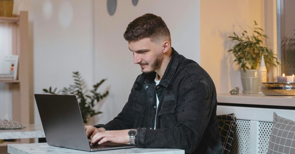283 A Caucasian man wearing black denim jacket smiling while using his laptop