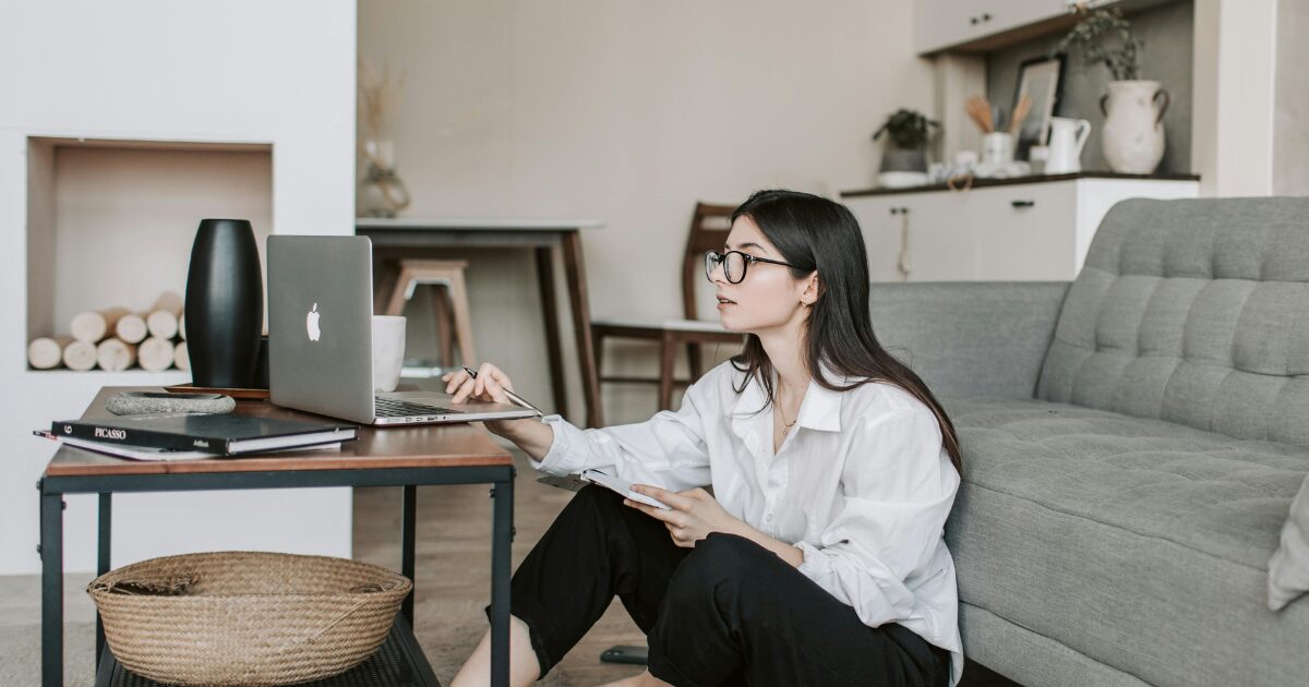 285 A Caucasian woman wearing a white blouse sitting on the floor while using her laptop on the table