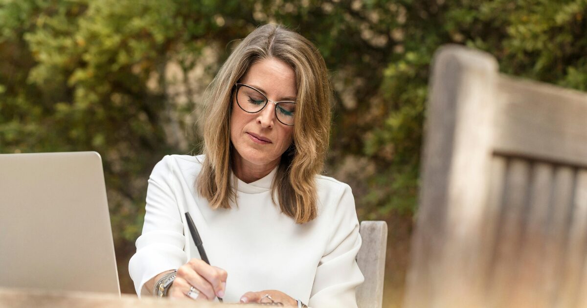 288 A Caucasian woman wearing a white blouse writing something down