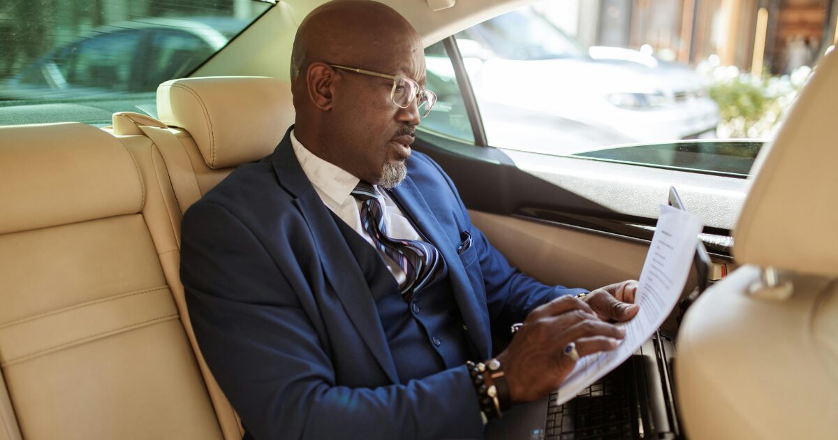 295 A Black man wearing a navy blue business suit while reading a document inside a vehicle