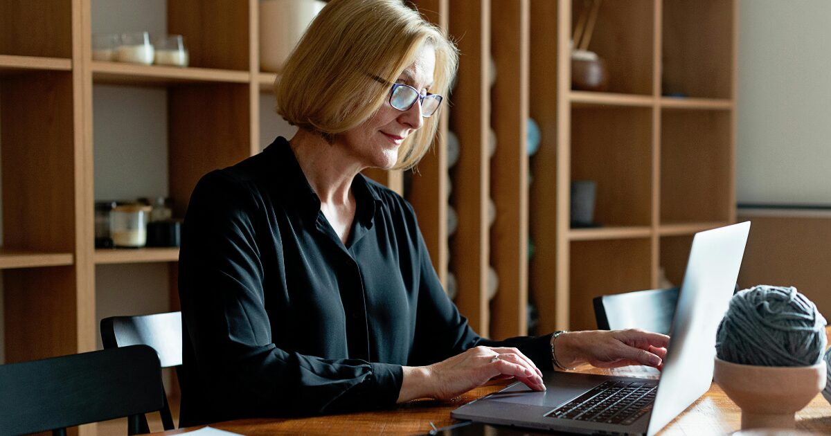 A Caucasian woman wearing a black buttoned long-sleeved blouse, using a laptop.