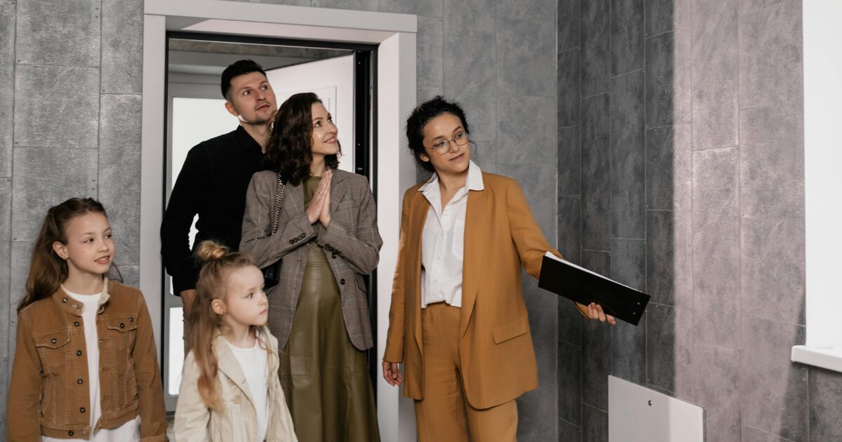 310 A Caucasian man and woman and two young Caucasian girls entering a room while being escorted by another Caucasian woman wearing a mustard blazer.