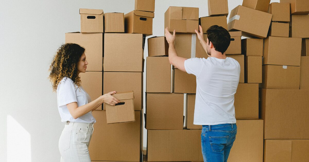 311 A Caucasian man and woman both wearing white t-shirts organizing cardboard moving boxes.