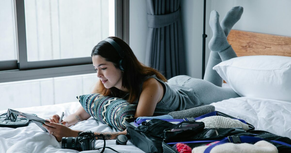320 A Caucasian woman wearing a gray sleeveless shirt, lying on the bed on her stomach while writing on a notebook
